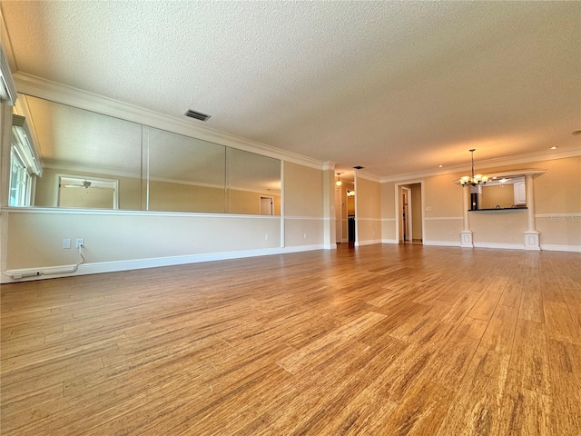 empty room with a notable chandelier, crown molding, and light wood-type flooring