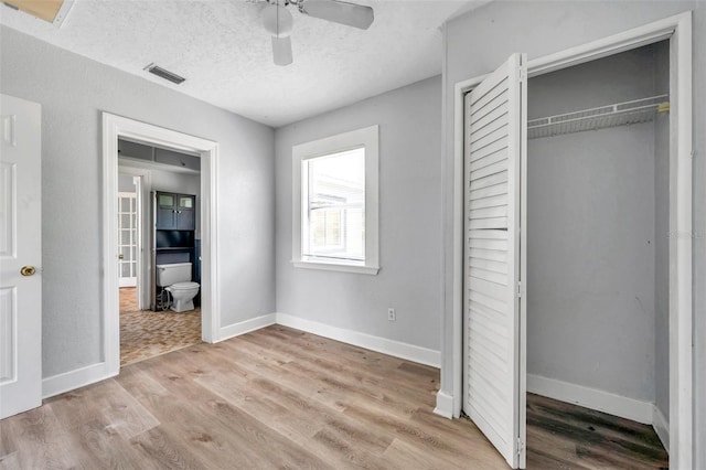 unfurnished bedroom featuring a textured ceiling, ceiling fan, light hardwood / wood-style floors, a closet, and ensuite bath