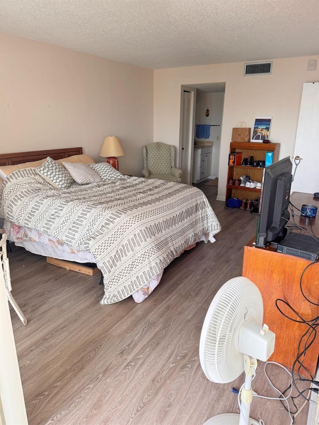 bedroom featuring hardwood / wood-style floors, a textured ceiling, and connected bathroom