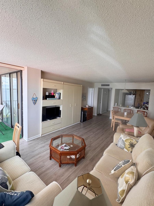 living area featuring a textured ceiling, wood finished floors, visible vents, and baseboards