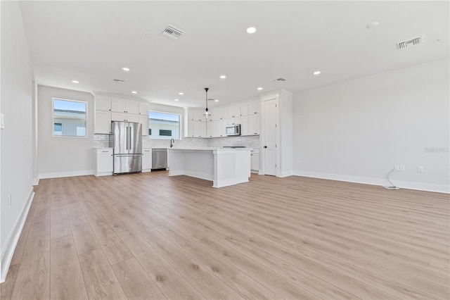 kitchen with appliances with stainless steel finishes, white cabinets, a center island, and pendant lighting