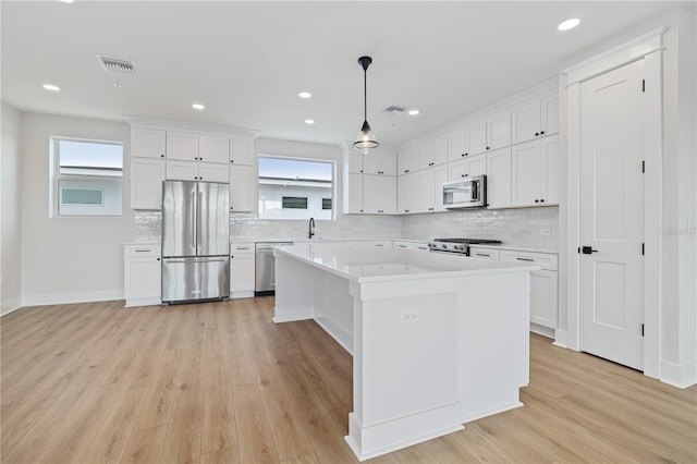 kitchen with light wood-type flooring, hanging light fixtures, a kitchen island, appliances with stainless steel finishes, and white cabinets