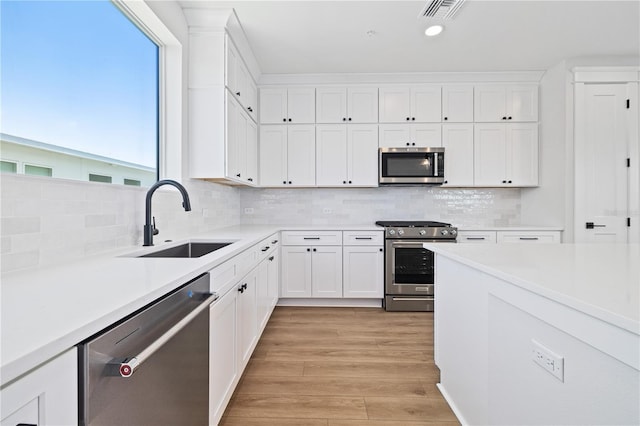 kitchen with light hardwood / wood-style flooring, stainless steel appliances, white cabinets, decorative backsplash, and sink