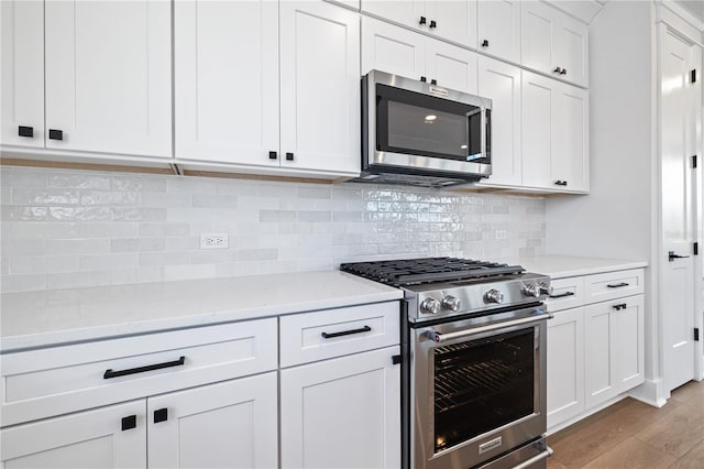 kitchen with appliances with stainless steel finishes, light stone countertops, white cabinets, backsplash, and light wood-type flooring