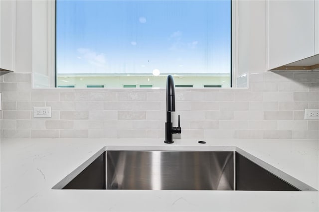 room details with white cabinets, sink, backsplash, and light stone counters