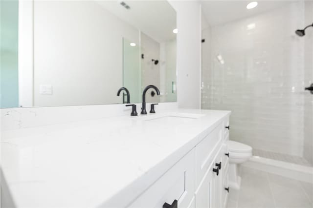 bathroom featuring vanity, a tile shower, toilet, and tile patterned floors