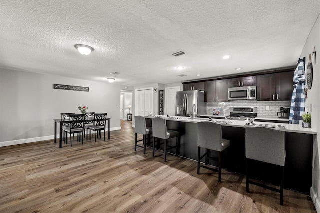 kitchen featuring hardwood / wood-style floors, dark brown cabinetry, stainless steel appliances, and decorative backsplash