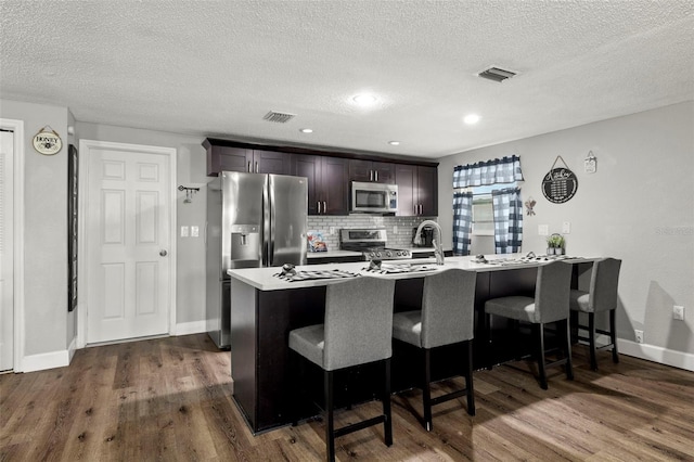 kitchen with a kitchen bar, appliances with stainless steel finishes, wood-type flooring, dark brown cabinets, and decorative backsplash