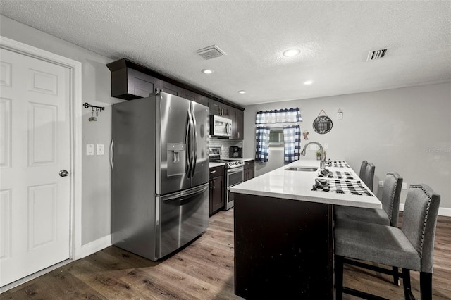 kitchen with stainless steel appliances, hardwood / wood-style floors, sink, a textured ceiling, and a breakfast bar area