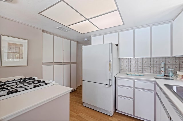 kitchen featuring white cabinets, decorative backsplash, light wood-type flooring, and white fridge