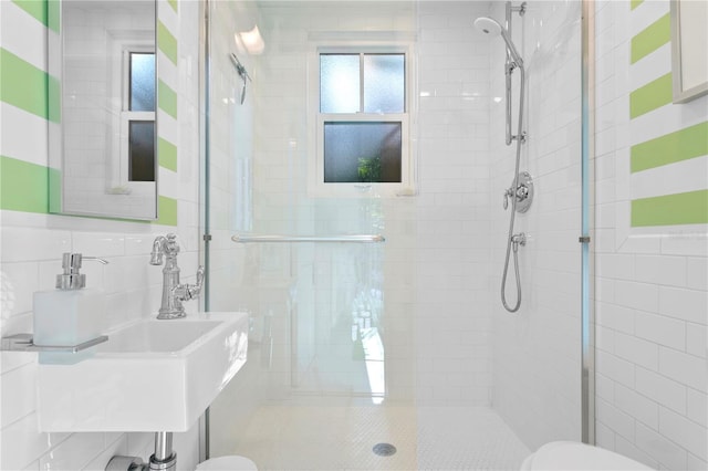 bathroom with a shower with shower door, sink, tile walls, and toilet