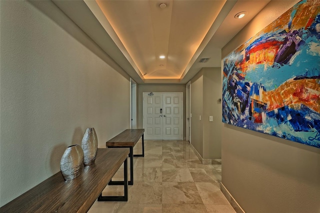 corridor featuring a tray ceiling and light tile patterned floors