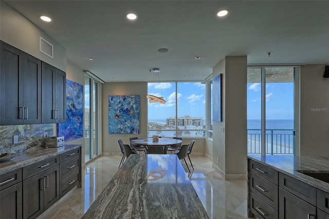 kitchen with tasteful backsplash, a water view, light tile patterned floors, and dark stone counters