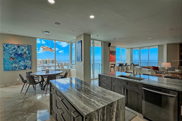 kitchen with a center island with sink, dishwasher, light stone countertops, a water view, and sink