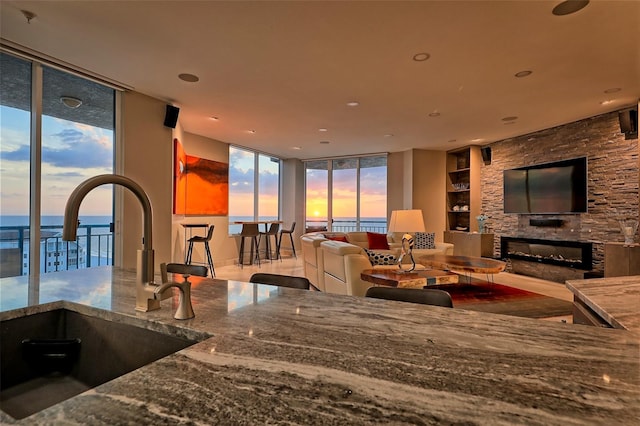 living room with sink, a water view, a wall of windows, and a stone fireplace