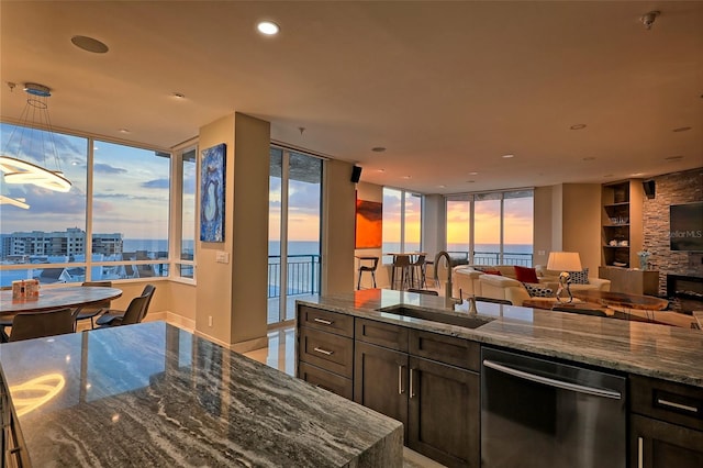 kitchen with stone counters, dark brown cabinets, a stone fireplace, stainless steel dishwasher, and sink