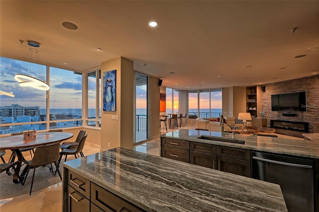 kitchen featuring stone counters, a water view, a fireplace, stainless steel dishwasher, and sink