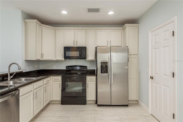 kitchen featuring cream cabinetry, sink, dark stone counters, and black appliances