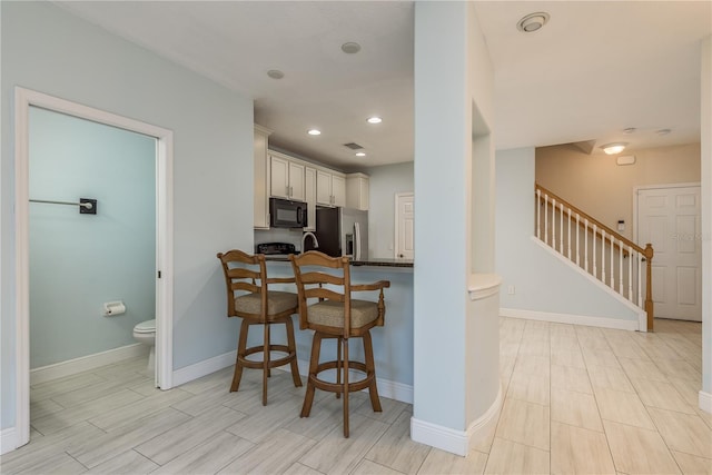 kitchen featuring sink, white cabinetry, a kitchen breakfast bar, stainless steel fridge with ice dispenser, and kitchen peninsula