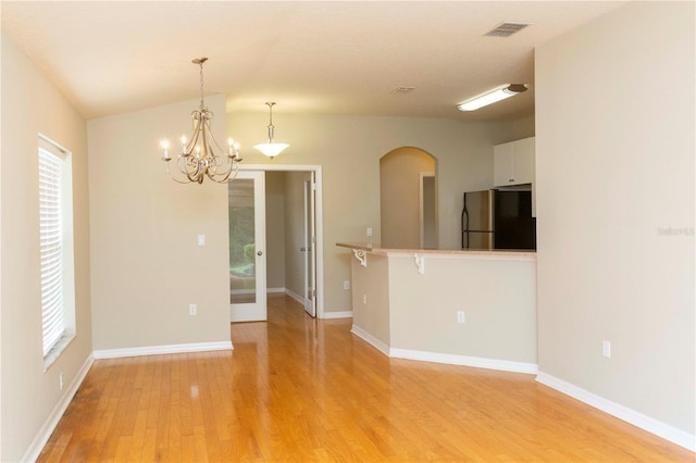 unfurnished room featuring lofted ceiling, an inviting chandelier, and light hardwood / wood-style flooring