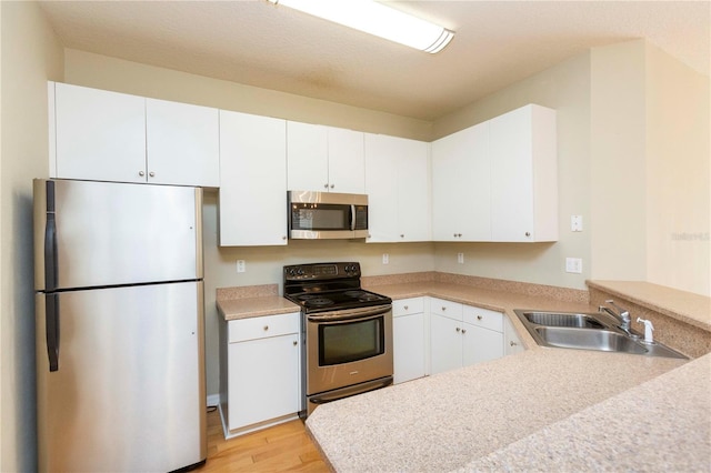 kitchen with light hardwood / wood-style flooring, stainless steel appliances, white cabinetry, sink, and kitchen peninsula