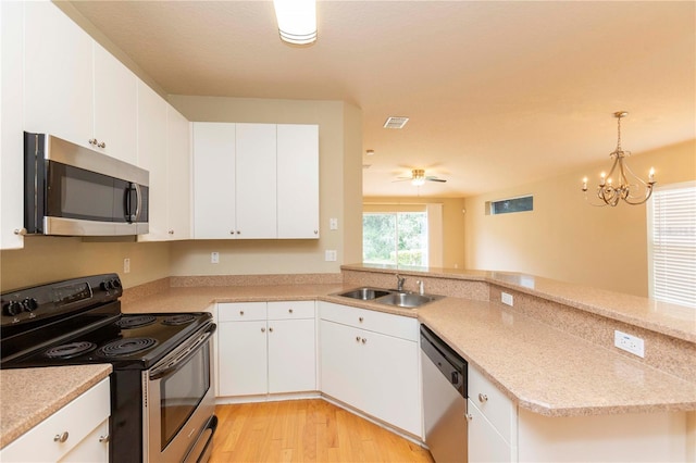 kitchen with a notable chandelier, stainless steel appliances, sink, kitchen peninsula, and white cabinetry