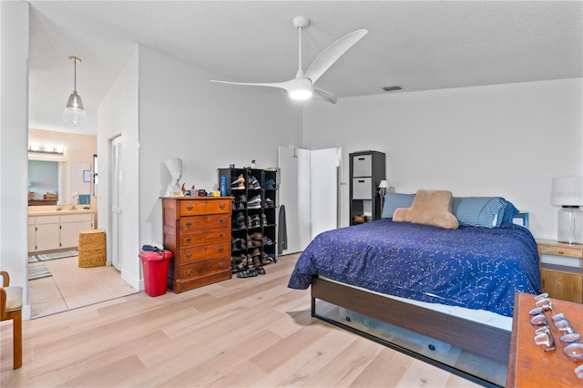 bedroom with light wood-type flooring, ceiling fan, connected bathroom, and a textured ceiling