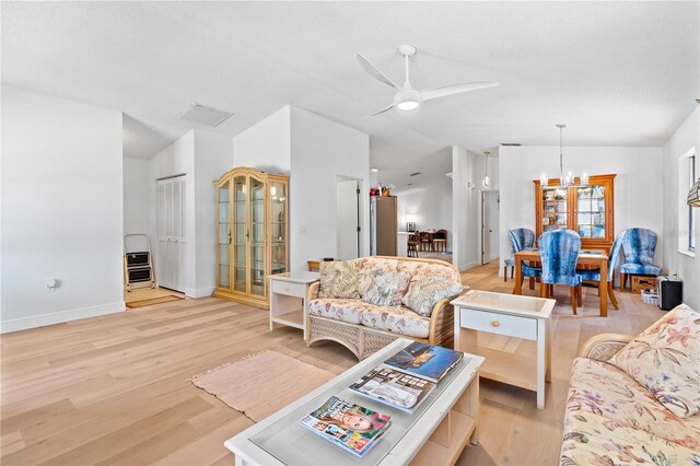 living room with ceiling fan with notable chandelier, vaulted ceiling, and light hardwood / wood-style floors