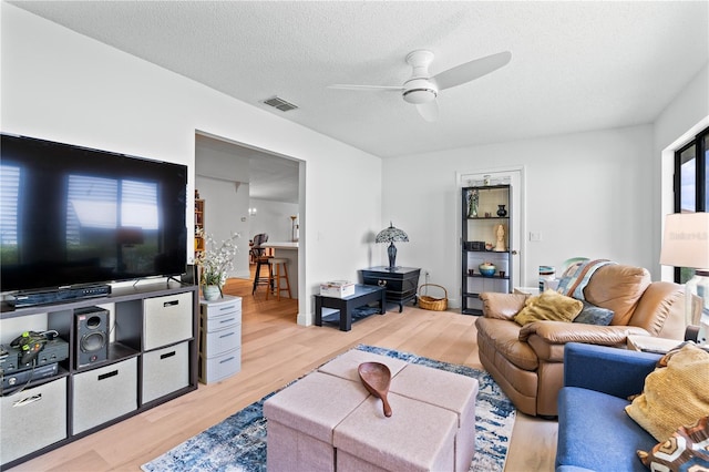 living room featuring light wood-type flooring, a textured ceiling, and ceiling fan