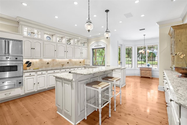 kitchen with decorative light fixtures, oven, tasteful backsplash, light wood-type flooring, and white cabinets