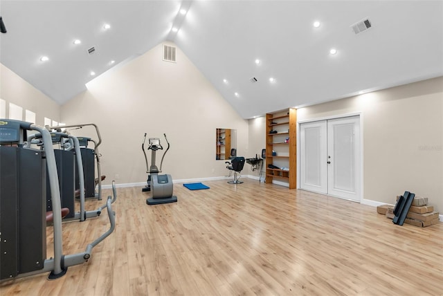 exercise room with high vaulted ceiling and light hardwood / wood-style flooring