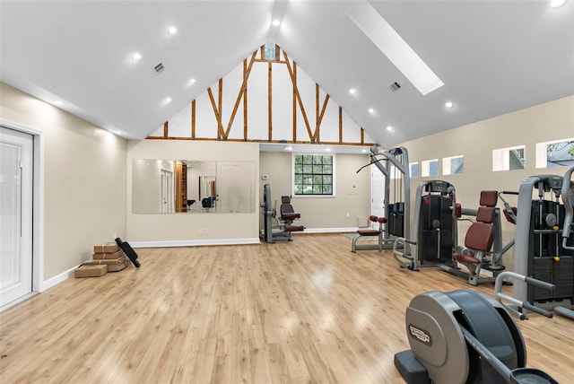 workout room with high vaulted ceiling, light hardwood / wood-style flooring, and a skylight