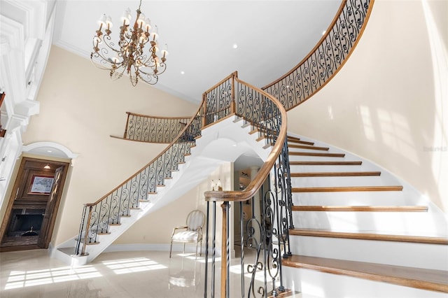 stairs with ornamental molding, a high ceiling, and an inviting chandelier