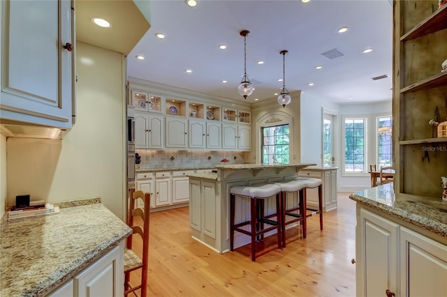 kitchen with decorative light fixtures, a kitchen island, light wood-type flooring, and a breakfast bar