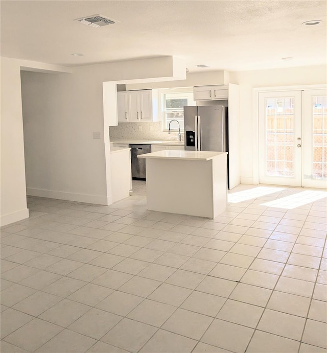 kitchen featuring white cabinetry, stainless steel appliances, a center island, backsplash, and light tile patterned floors