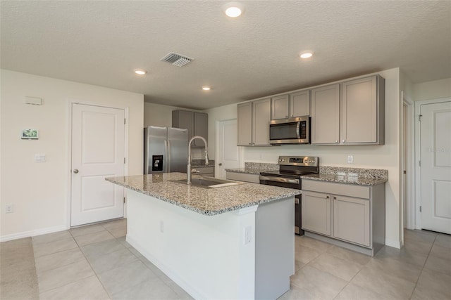 kitchen featuring gray cabinets, light tile patterned flooring, appliances with stainless steel finishes, an island with sink, and sink