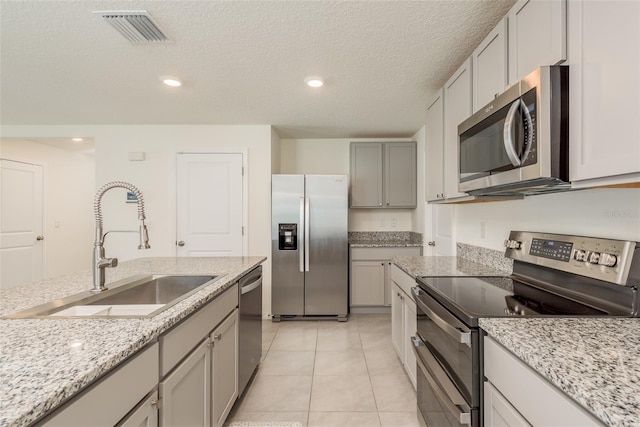 kitchen with a textured ceiling, appliances with stainless steel finishes, light stone countertops, light tile patterned flooring, and sink