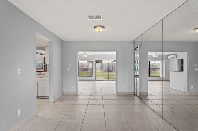 interior space with a wall mounted air conditioner, ceiling fan, light tile patterned flooring, and a textured ceiling