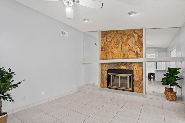 unfurnished living room with ceiling fan, a stone fireplace, a textured ceiling, vaulted ceiling, and light tile patterned flooring