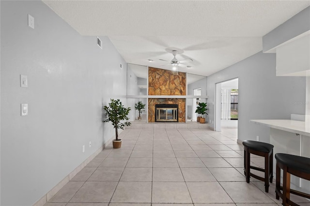 living room featuring vaulted ceiling, ceiling fan, light tile patterned floors, a textured ceiling, and a fireplace