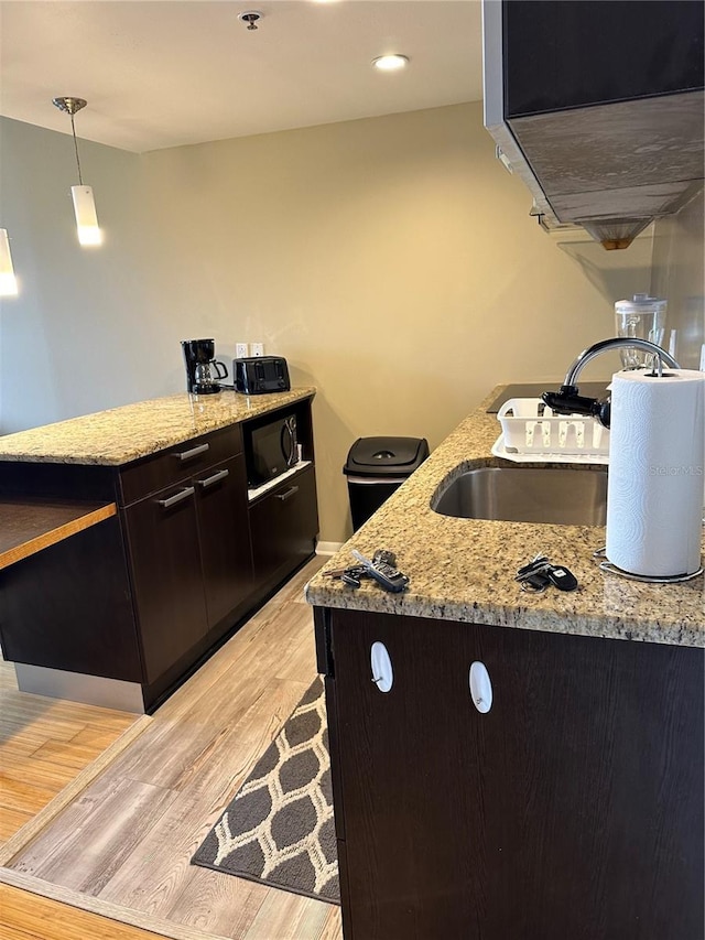 kitchen with hanging light fixtures, dark brown cabinets, black microwave, light hardwood / wood-style floors, and light stone counters