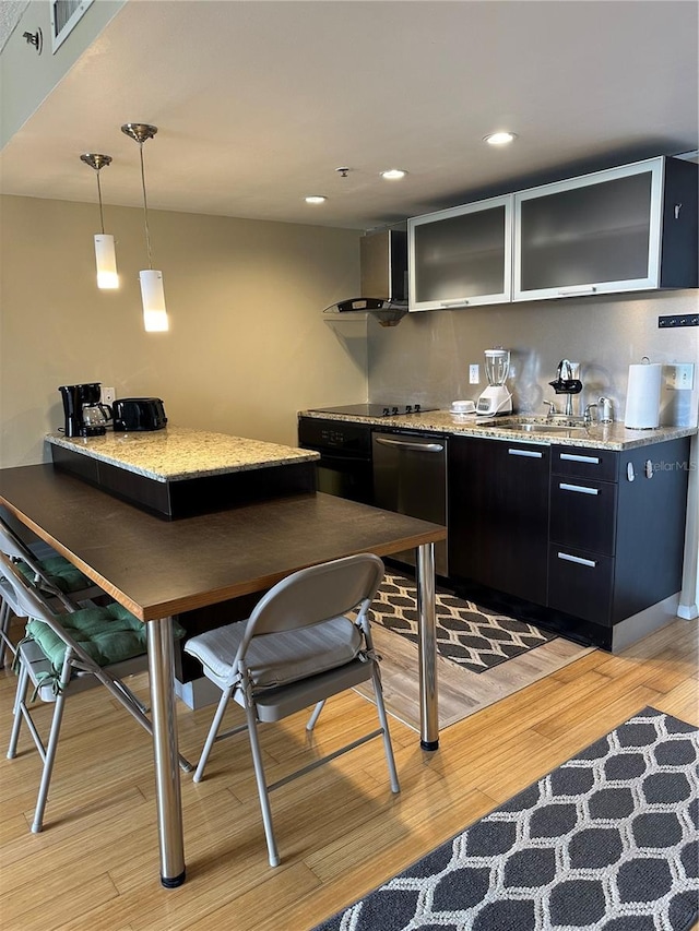 kitchen with dishwasher, pendant lighting, wall chimney exhaust hood, light stone countertops, and light wood-type flooring