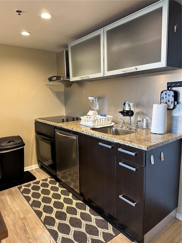 kitchen with light wood-type flooring, light stone counters, black appliances, sink, and wall chimney exhaust hood