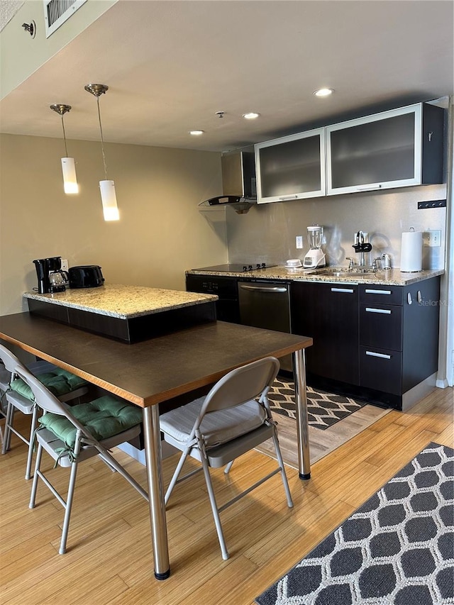 interior space featuring wall chimney range hood, light wood-type flooring, light stone counters, and hanging light fixtures