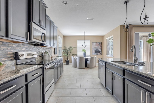 kitchen with sink, tasteful backsplash, light stone counters, pendant lighting, and appliances with stainless steel finishes