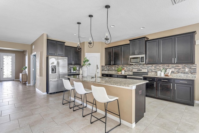 kitchen with backsplash, sink, stainless steel appliances, and a center island with sink