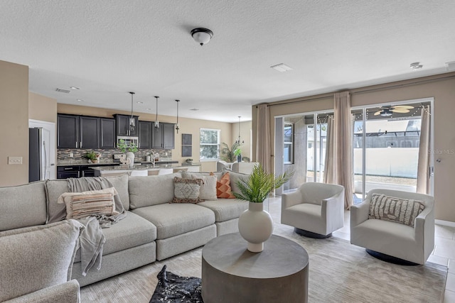 tiled living room with ceiling fan, sink, and a textured ceiling