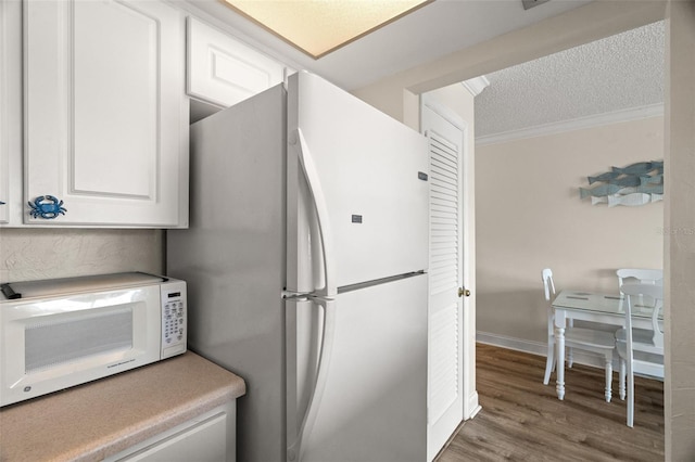 kitchen with white appliances, a textured ceiling, hardwood / wood-style floors, white cabinets, and crown molding