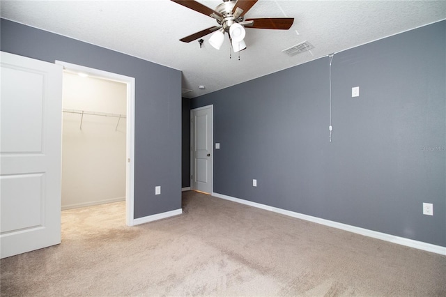 unfurnished bedroom with ceiling fan, a spacious closet, a textured ceiling, light colored carpet, and a closet