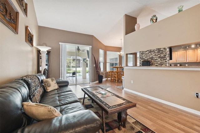 living room featuring a towering ceiling, ceiling fan with notable chandelier, and light hardwood / wood-style flooring